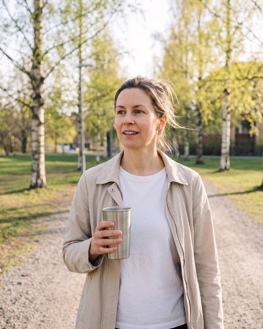 Samma kvinna på promenad i en park på våren med en kaffemugg i handen
